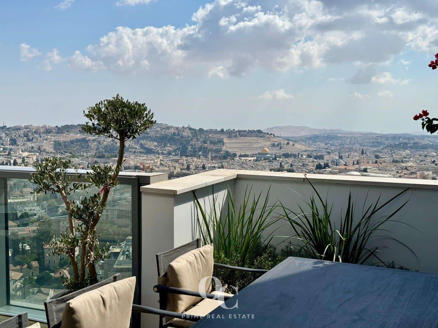 The actual view across the penthouse balcony railing, with the Temple Mount, golden Dome of the Rock, and Mount of Olives beyond the terrace plants and dining chairs